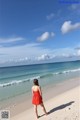 A woman in a red dress walking on the beach.