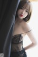 A woman in a black lingerie leaning against a curtain.