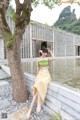 A woman in a yellow skirt sitting on a stone wall next to a tree.