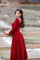 A woman in a red dress leaning on a wooden railing.