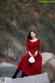 A woman in a red dress sitting on a rock.