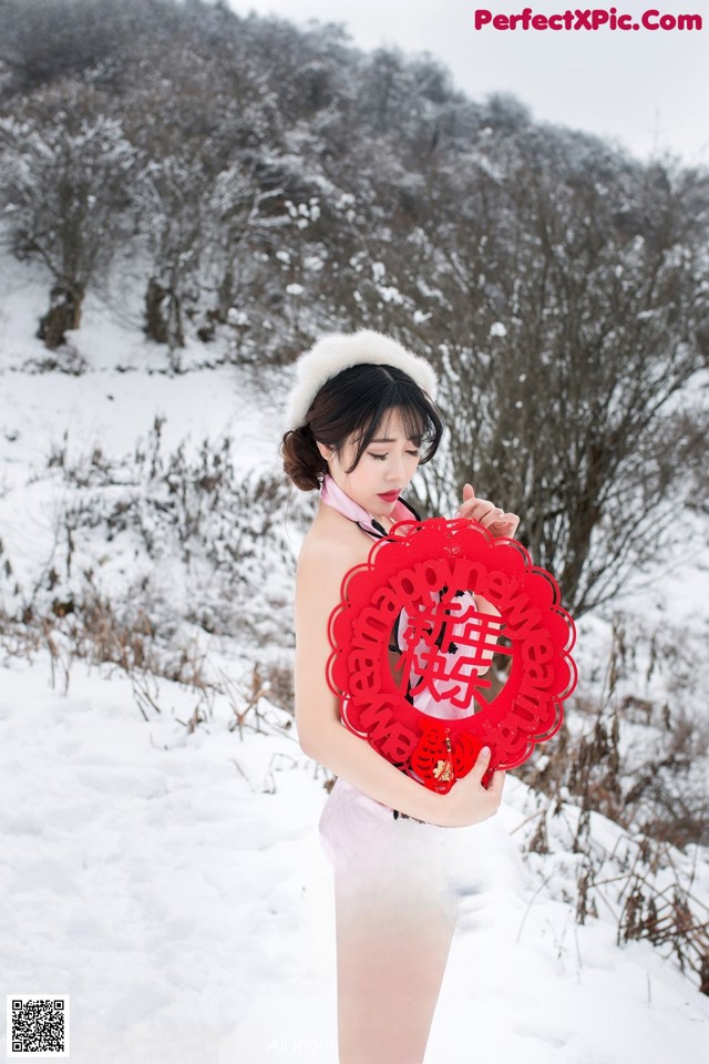 A woman in a pink dress holding a red heart in the snow.