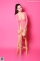 A woman in a pink bodysuit sitting on a wooden stool.