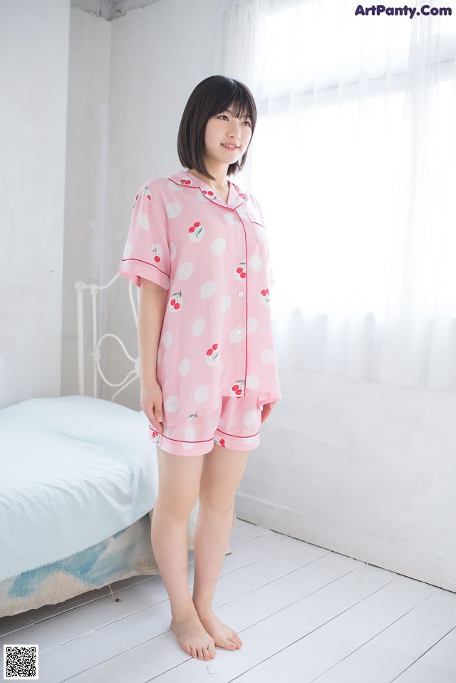 A woman standing in front of a bed wearing a pink pajamas.