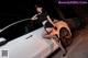 A woman posing next to a white car at night.