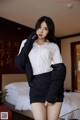 A woman in a white shirt and black skirt posing on a bed.