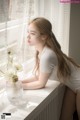 A woman sitting on a window sill next to a vase of flowers.