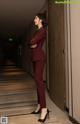 A woman in a red suit standing in a hallway.