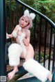 A woman in a white furry outfit is posing on a railing.