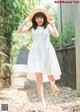 A woman in a white dress and straw hat walking down a path.