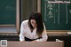 A woman sitting at a desk in front of a blackboard.