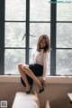 A woman sitting on a window sill in a white shirt and black skirt.