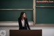 A woman standing at a podium in front of a blackboard.